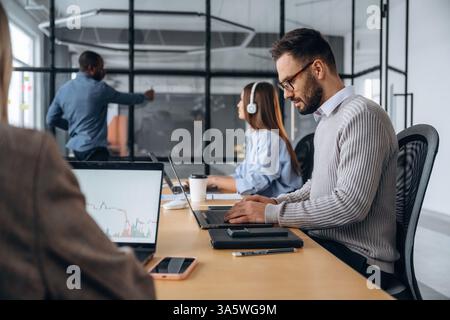Focused, sitting by laptop. Professional workers are in the modern office together. Stock Photo
