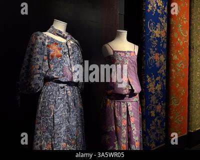 The image shows batik dresses on mannequins. The dresses are made of colorful fabric with floral patterns. Next to the dresses are fabric rolls. Stock Photo