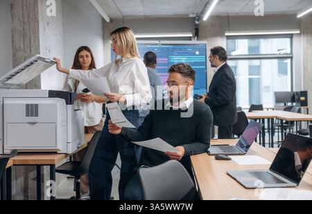 Using printer. Group of office workers are indoors together. Stock Photo