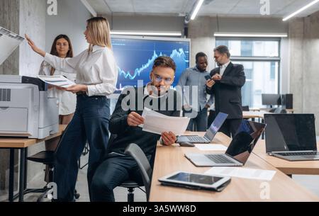 Using printer. Group of office workers are indoors together. Stock Photo