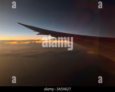 View of airplane wing over clouds at dusk from passenger window. Stock Photo