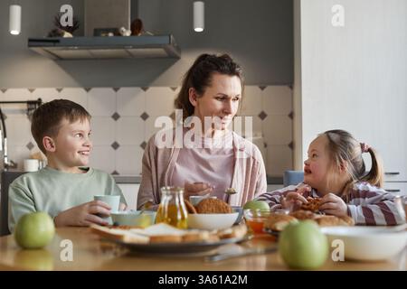 Portrait of mother looking at girl with down syndrome while sitting at dining table and enjoying breakfast together with family, copy space Stock Photo