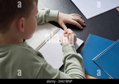 High angle close up of boy writing in notebook while doing homework or studying at desk, copy space Stock Photo