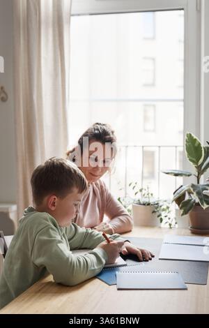 Vertical side view portrait of caring single mother helping son doing homework in cozy home interior, copy space Stock Photo
