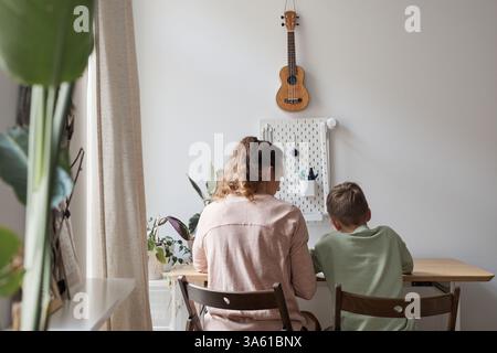 Back view portrait of caring single mother helping son doing homework in cozy home interior, copy space Stock Photo