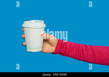 Woman hand holding a disposable coffee cup with a white lid on a vibrant blue background Stock Photo