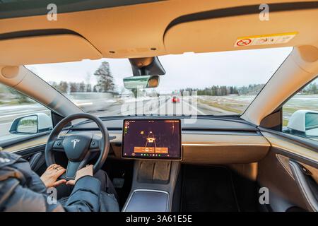 Interior of Tesla Model Y with driver using autopilot on highway through snowy winter landscape. Sweden. Stock Photo