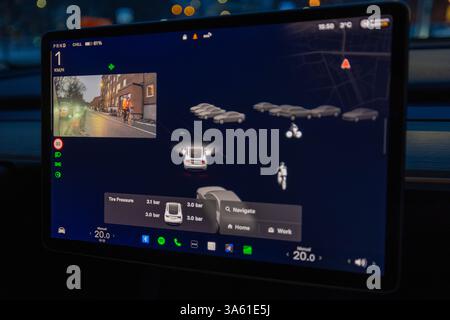 Tesla Model Y touchscreen displaying autopilot interface with cyclist and road obstacles in evening traffic. Sweden. Stock Photo