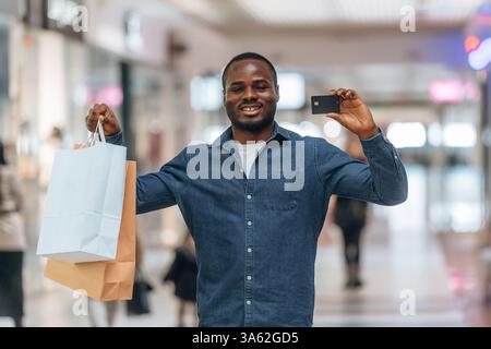 Successful payment, holding credit card. Black man is in the hall of the supermarket. Stock Photo