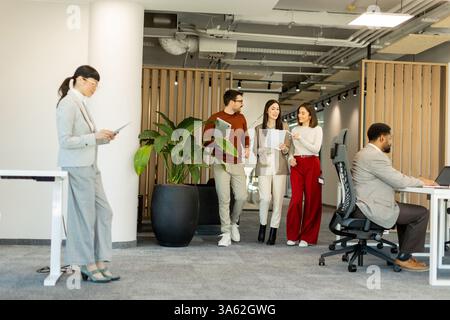 A group of professionals engages in lively discussions while reviewing documents, embodying teamwork and creativity in a bright, contemporary workspac Stock Photo