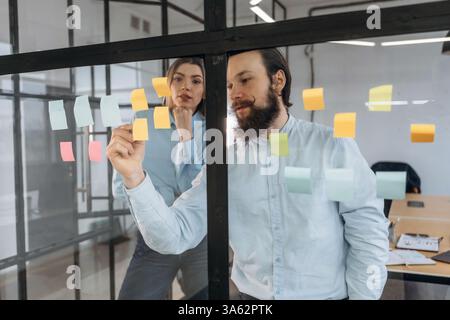 Stickers on glass, standing. Man and woman are in the office together. Stock Photo