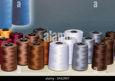 Spools of colorful thread in various shades create a lively display in a sewing studio. The setup reflects creativity and craft, inviting inspiration Stock Photo
