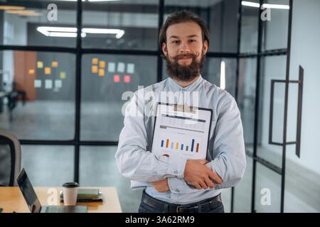 Standing, holding documents and smiling. Businessman is working in the office. Stock Photo