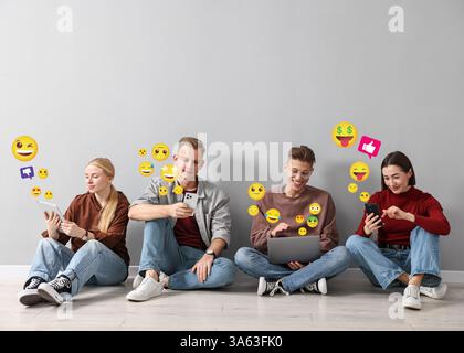 Social media. Group of young people using different gadgets on light grey background. Different notification signs and emojis near them Stock Photo