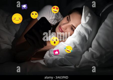 Social media. Woman using mobile phone in bed at night. Different notification signs and emojis near gadget Stock Photo