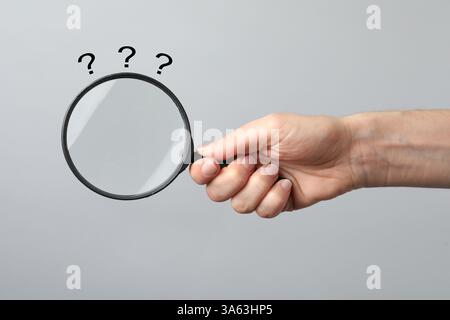 Question marks and woman with magnifying glass on grey background, closeup Stock Photo