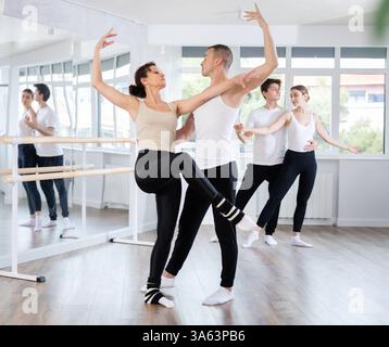 Happy contemporary ballet dancers couple dressed in black and white performing graceful choreography in hall with ballet bar Stock Photo