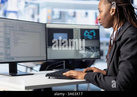 Programmer in photovoltaics facility using PC program to diagnose malfunctioning systems. African american woman coding at computer desk in solar panels manufacturing plant, reducing downtime Stock Photo