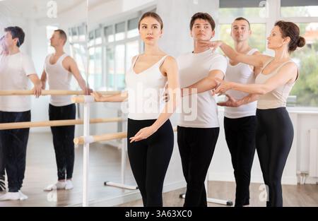 Group of ballet enthusiasts practicing at barre with experienced ballerina Stock Photo