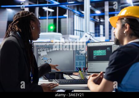 Teamworking photovoltaics factory colleagues using tablet to do finetuning of system settings for maximum efficiency. Engineering team looking at solar panel assembly lines configuration on PC Stock Photo