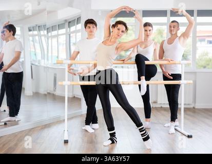 Group of adult students of ballet class posing at barre in studio Stock Photo