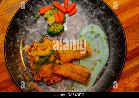 Fried fish fillet with vegetables and sauce on a beautiful plate on a wooden table in a restaurant. dishes from the menu. new cooking recipe. view Stock Photo