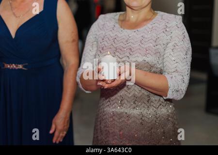 The parents of the newlyweds hold a burning candle in their hands to light the family hearth at the wedding ceremony. Stock Photo