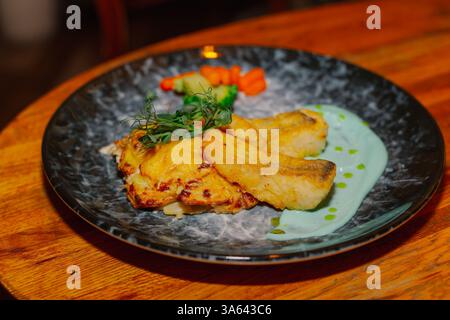 Fried fish fillet with vegetables and sauce on a beautiful plate on a wooden table in a restaurant. dishes from the menu Stock Photo