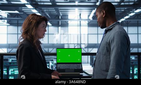 Data center team of computer scientists using mockup laptop to review equipment diagnostics. Teamworking IT experts adjusting server room configurations using chroma key notebook, camera B Stock Photo