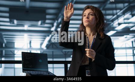 Technicians in high tech AI data center workspace looking at hologram visualization. Programmer working on securing server room hardware using AR artificial intelligence tech, camera A Stock Photo