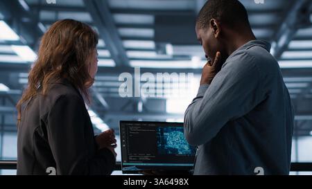 Software developers in data center using laptop, employing AI machine learning models. Workers using notebook to fulfill artificial intelligence infrastructure needs, allocating resources, camera A Stock Photo