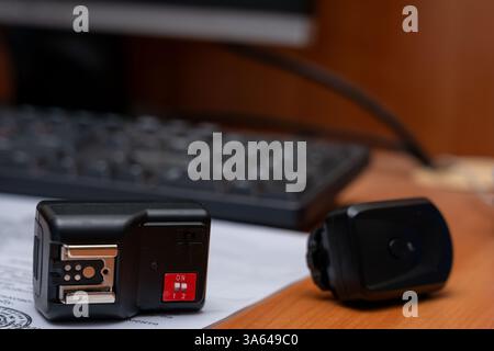 A remote control device rests on a wooden desk next to a computer keyboard, with paperwork scattered nearby. The setup suggests an office or study env Stock Photo