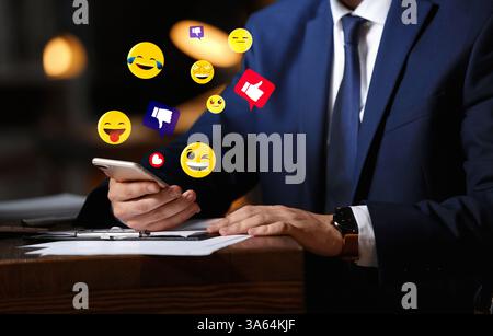 Social media. Businessman using mobile phone in office, closeup. Different notification signs and emojis near gadget Stock Photo