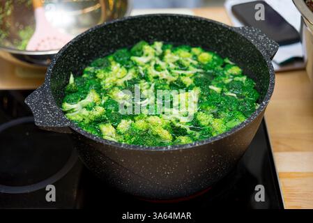 Fresh broccoli florets boiling in a black speckled cooking pot on an induction stove, preparing a healthy vegetable dish. Stock Photo
