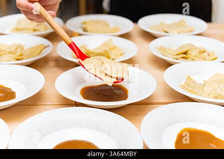 A chef plates freshly cooked ravioli onto white dishes with sauce, using a red spoon, preparing an elegant pasta dish. Stock Photo