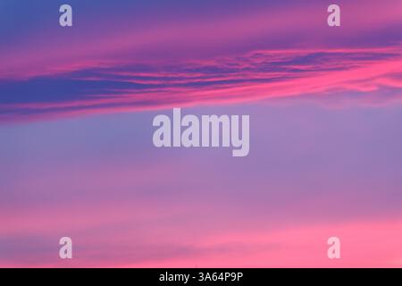 Pink hues color dusk cloudscape on soft blue background. Two gently curving pink lines sandwich baby blue daylight sky slipping away into night. Stock Photo