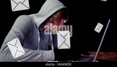 Young man in hoodie using laptop, surrounded by floating email icons Stock Photo