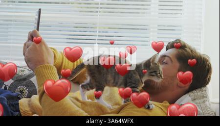 Relaxing at home, young man taking selfie with playful kitten on couch Stock Photo