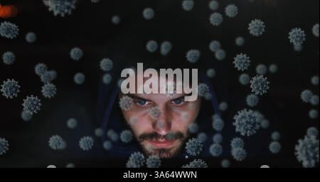 Man in hoodie surrounded by digital virus graphics, focused and serious Stock Photo