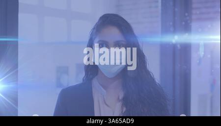 Blue light trails against portrait of indian woman wearing facemask at office Stock Photo