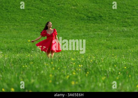 Smiling young woman spins and dances on a green grass meadow at sunset Stock Photo