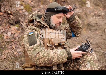 Ukrainian Army operator in FPV glasses controls drone with bomb to drop to enemy. Concept modern war with technology airplane robots. Stock Photo