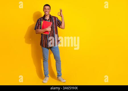 Young stylish male student in casual fashion outfit holding folder against vivid yellow backdrop with trendy and confident gesture Stock Photo