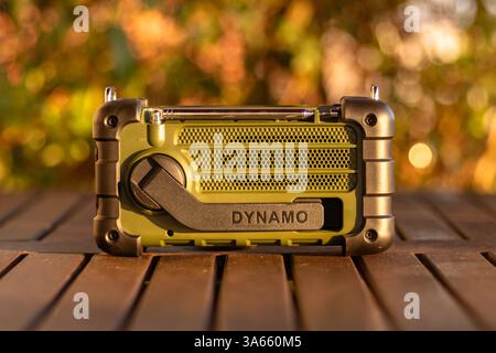 A green and black hand-crank dynamo radio sits on an outdoor surface with a blurred natural background, ideal for emergencies, outdoor adventures, or Stock Photo