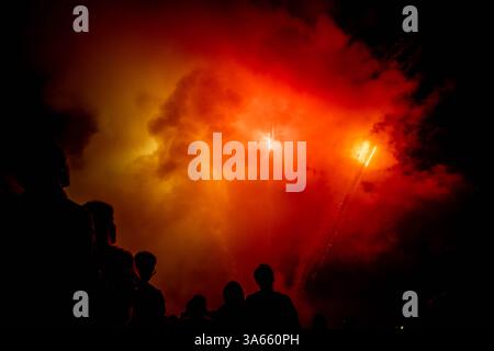 A group of Americans are seen together in silhouette watching a fireworks display light up the hot summertime night sky on the 4th of July Stock Photo