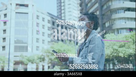 Image of multiple changing numbers floating against woman wearing face mask using smartphone Stock Photo