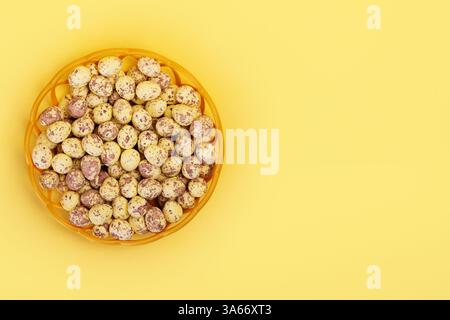 Top view of wicker basket full of painted small easter eggs on vibrant yellow table with copy space Stock Photo