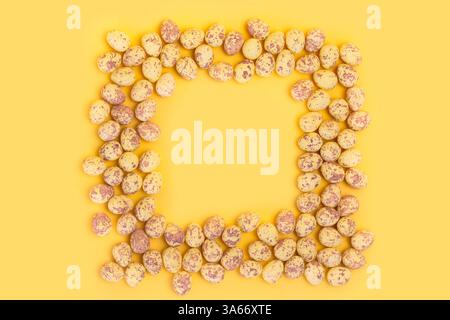 Small quail eggs shaped into square isolated on plain yellow background Stock Photo