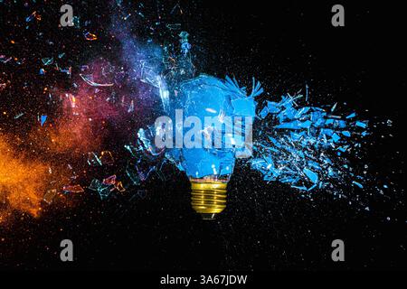Blue lightbulb exploding on black background with colorful powder Stock Photo