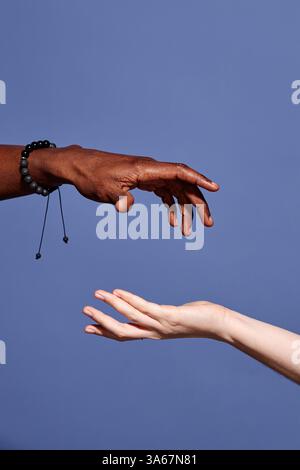 Close-up of two hands, one with darker skin and another with lighter skin, reaching towards each other against blue background, demonstrating diversity and connection Stock Photo